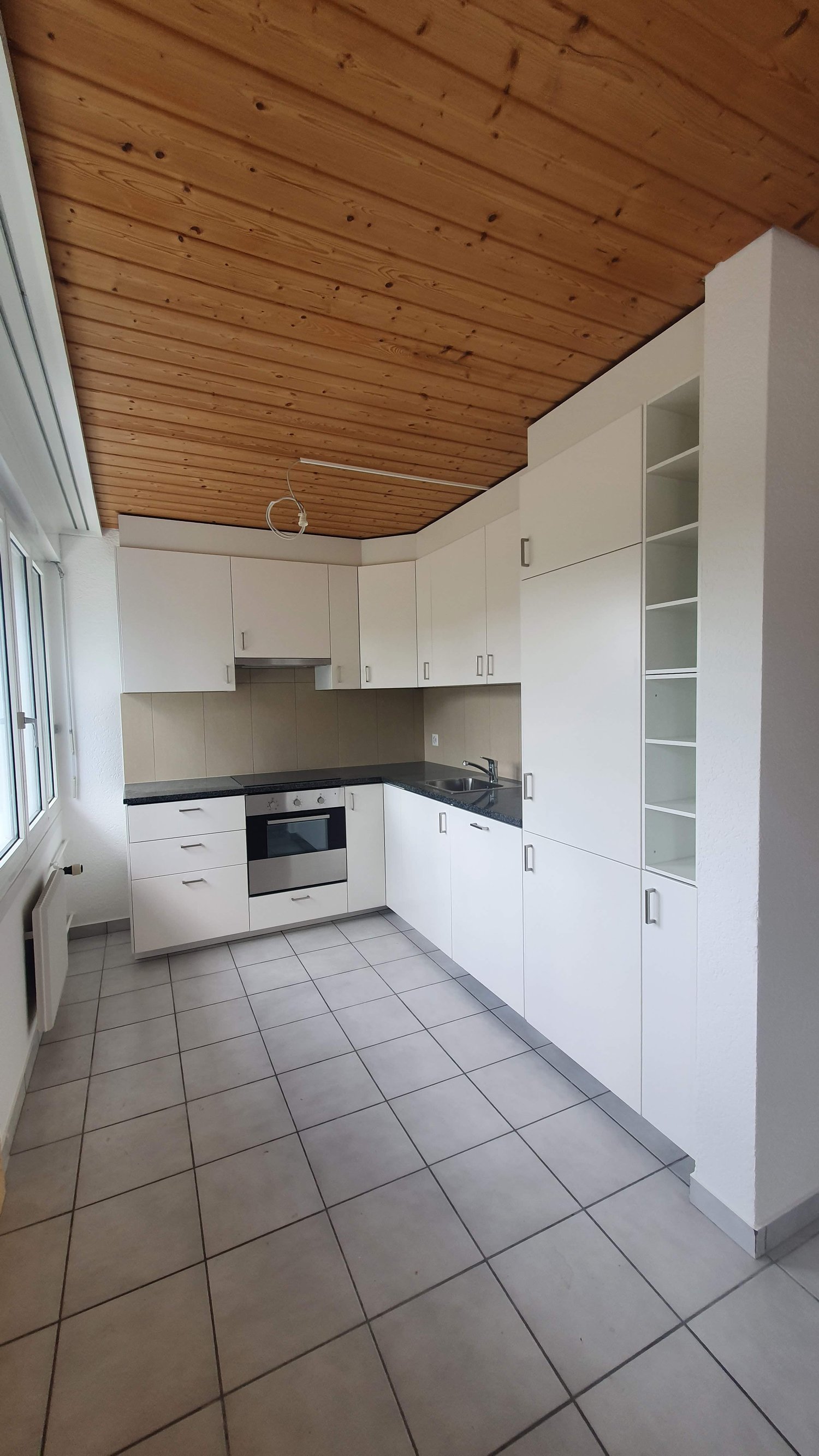 Modern kitchen with white cabinetry, tiled flooring, modern appliances, wooden ceiling