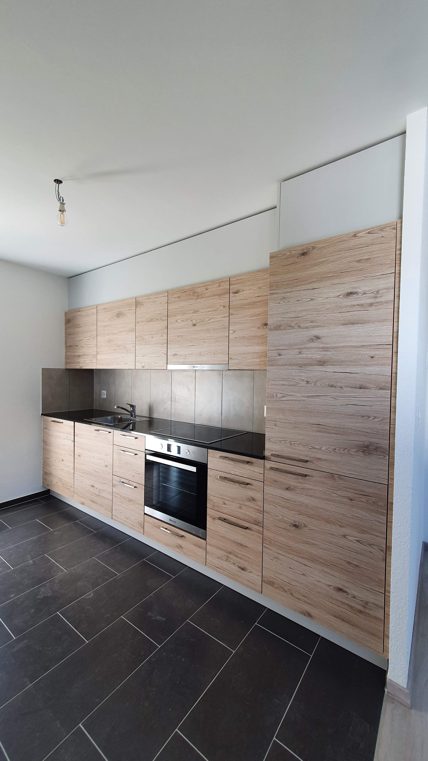 Modern and minimalistic kitchen with wooden cabinets, black countertops, built-in oven and sink with faucet, light fixtures