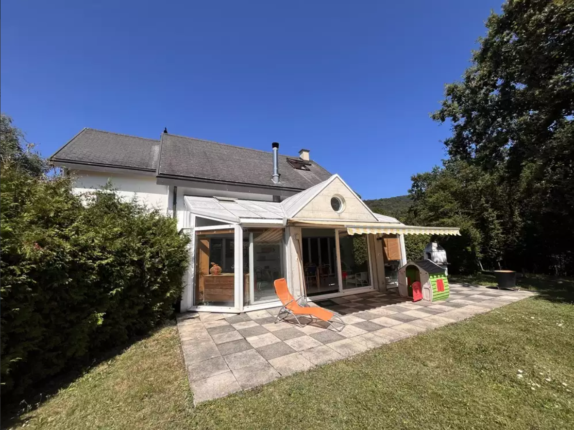 white house, gray roof, glass doors, tiled patio, orange chair, green bush, clear sky, backyard, no visible garage or swimming pool