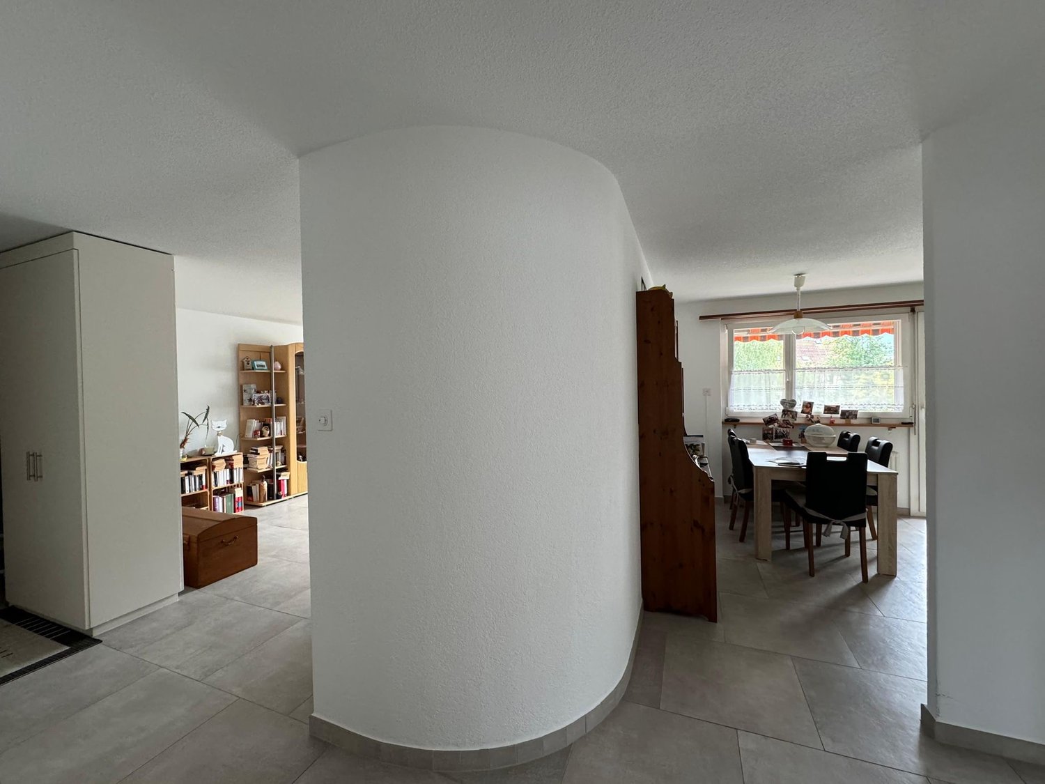Empty room with a curved wall, a cabinet, a table, and a window.