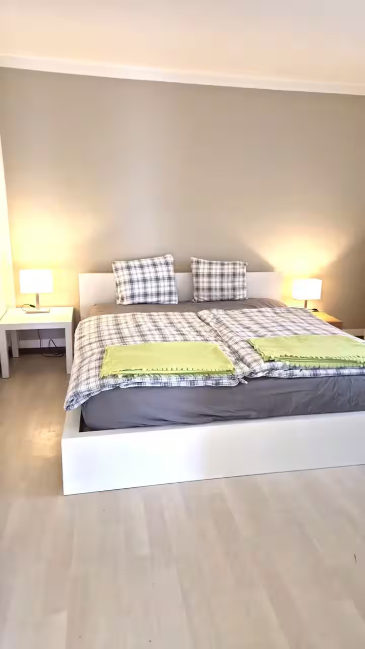 double bed with blanket, bedspread, night stand with lamp, wooden floor, grey wall