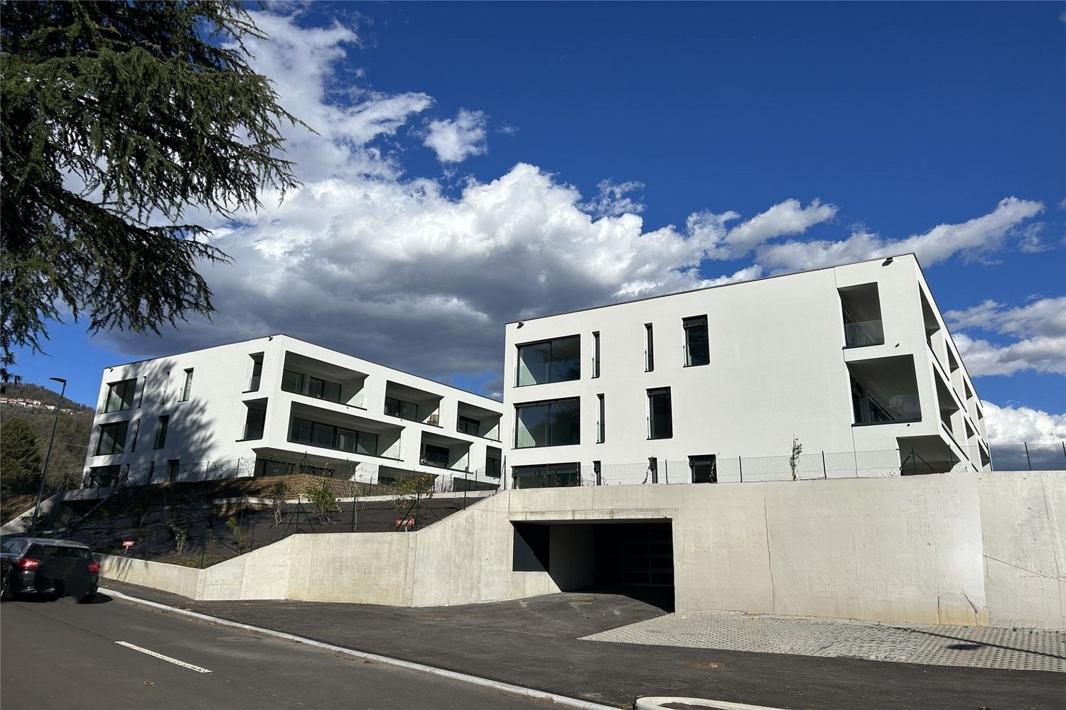 Modern apartment building, white exterior, large windows, balconies, underground parking