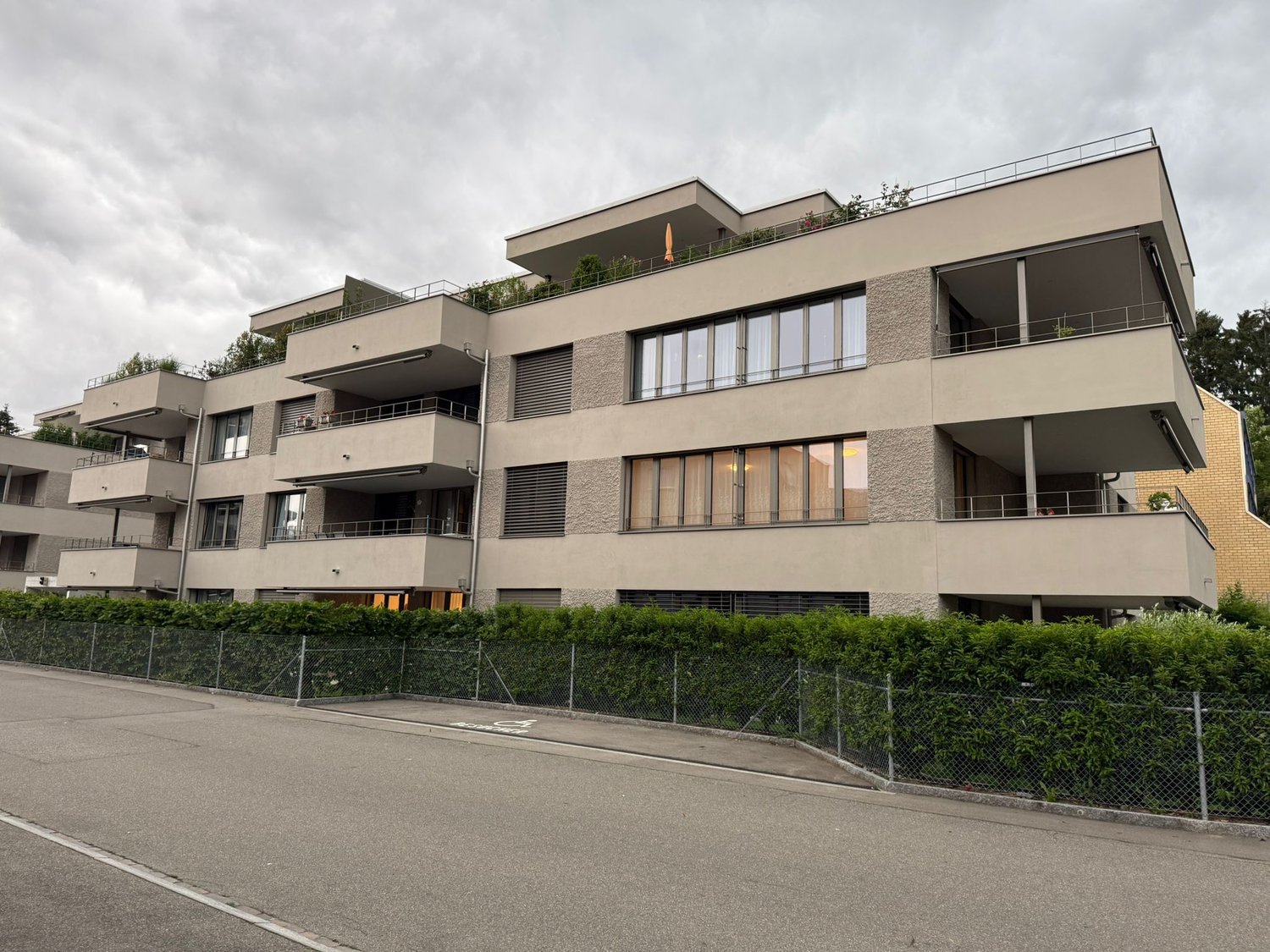 Multi-story building, balconies, large windows, fenced hedge