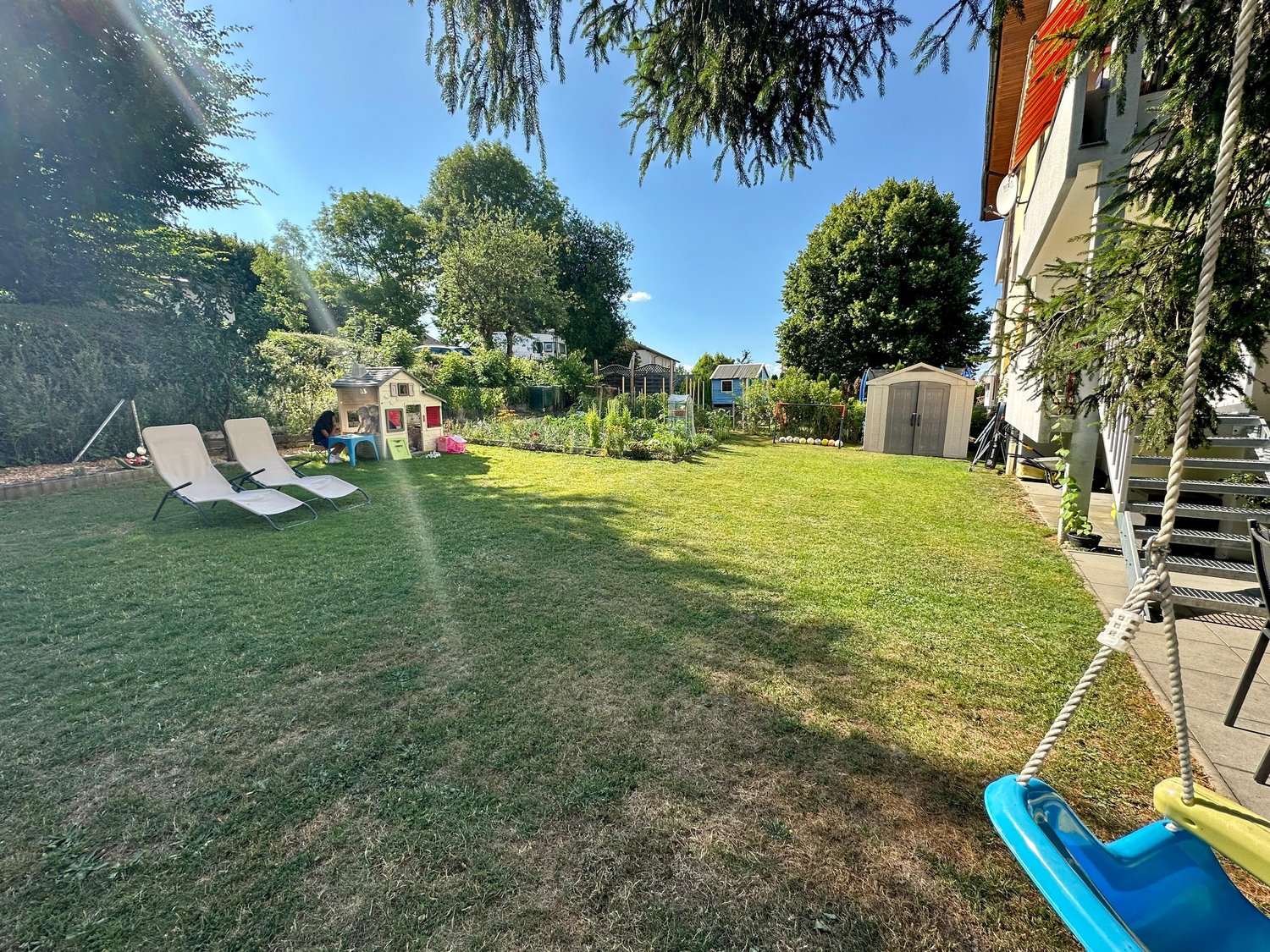 Large open garden, white sun loungers, swing, small tree house, green trees, well-maintained grass