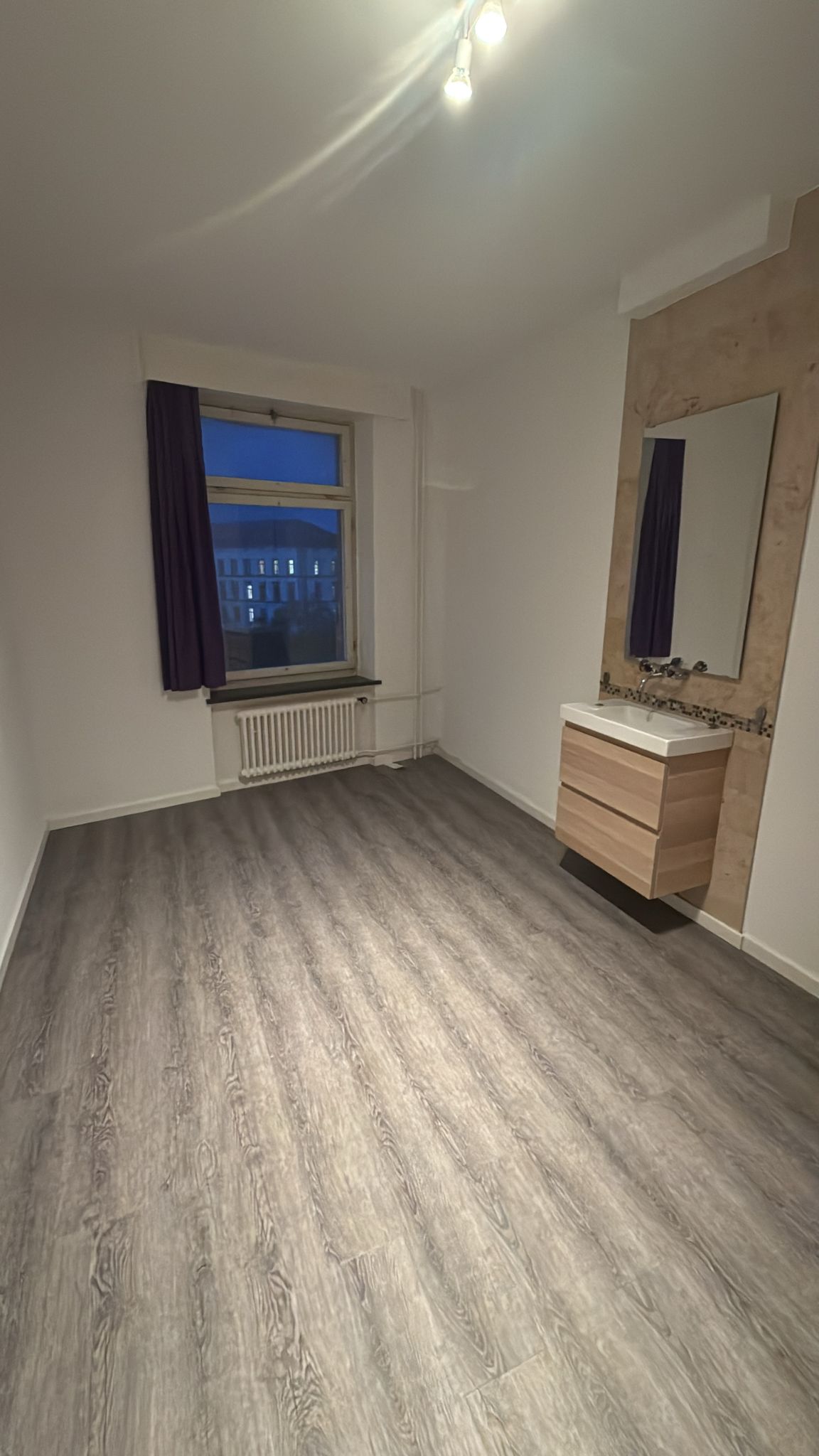 bathroom with wooden flooring, window with curtain, mirror, wooden sink, radiator, ceiling lights