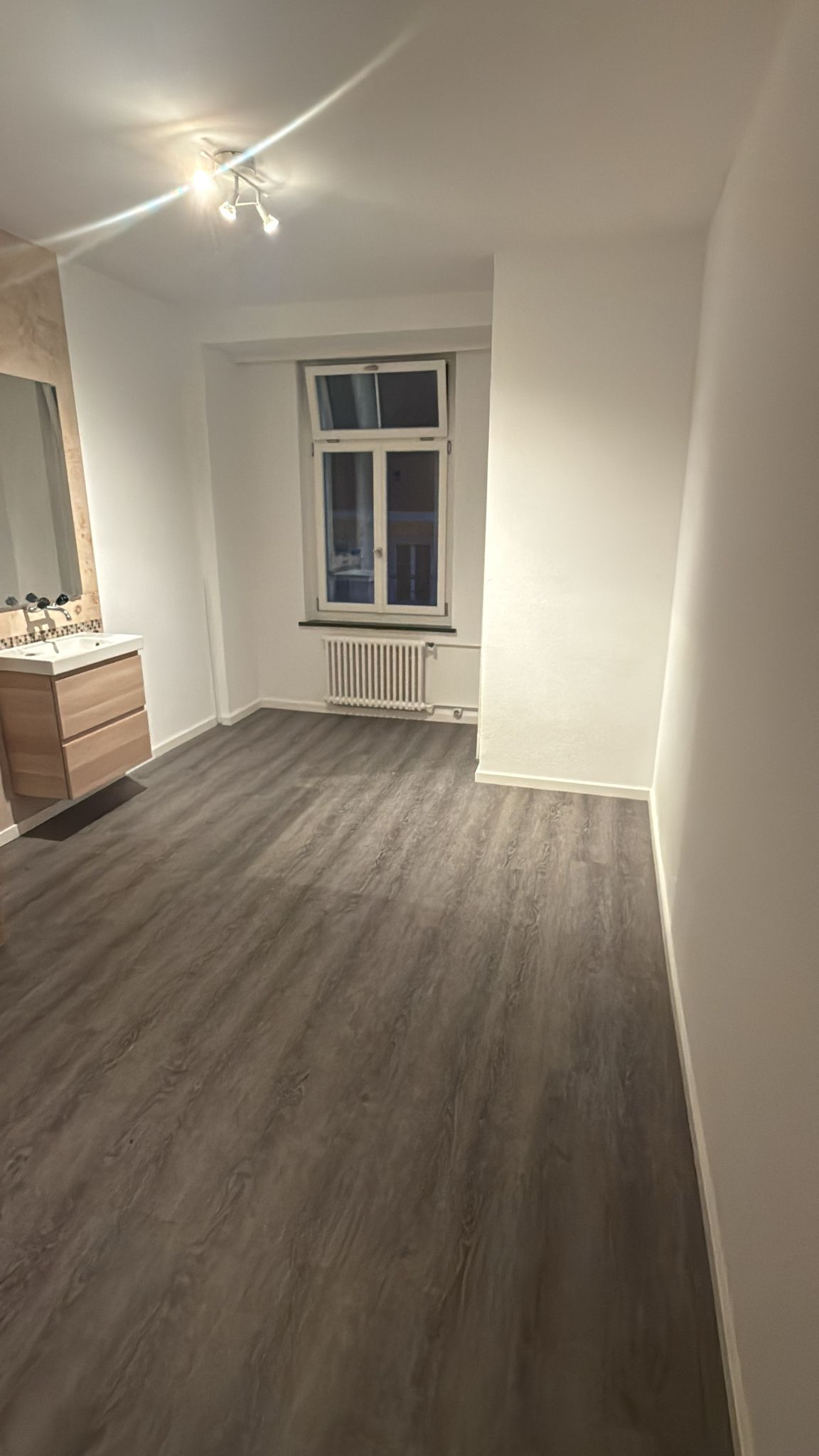 empty room, wooden floor, bathroom sink, mirror, window, radiator