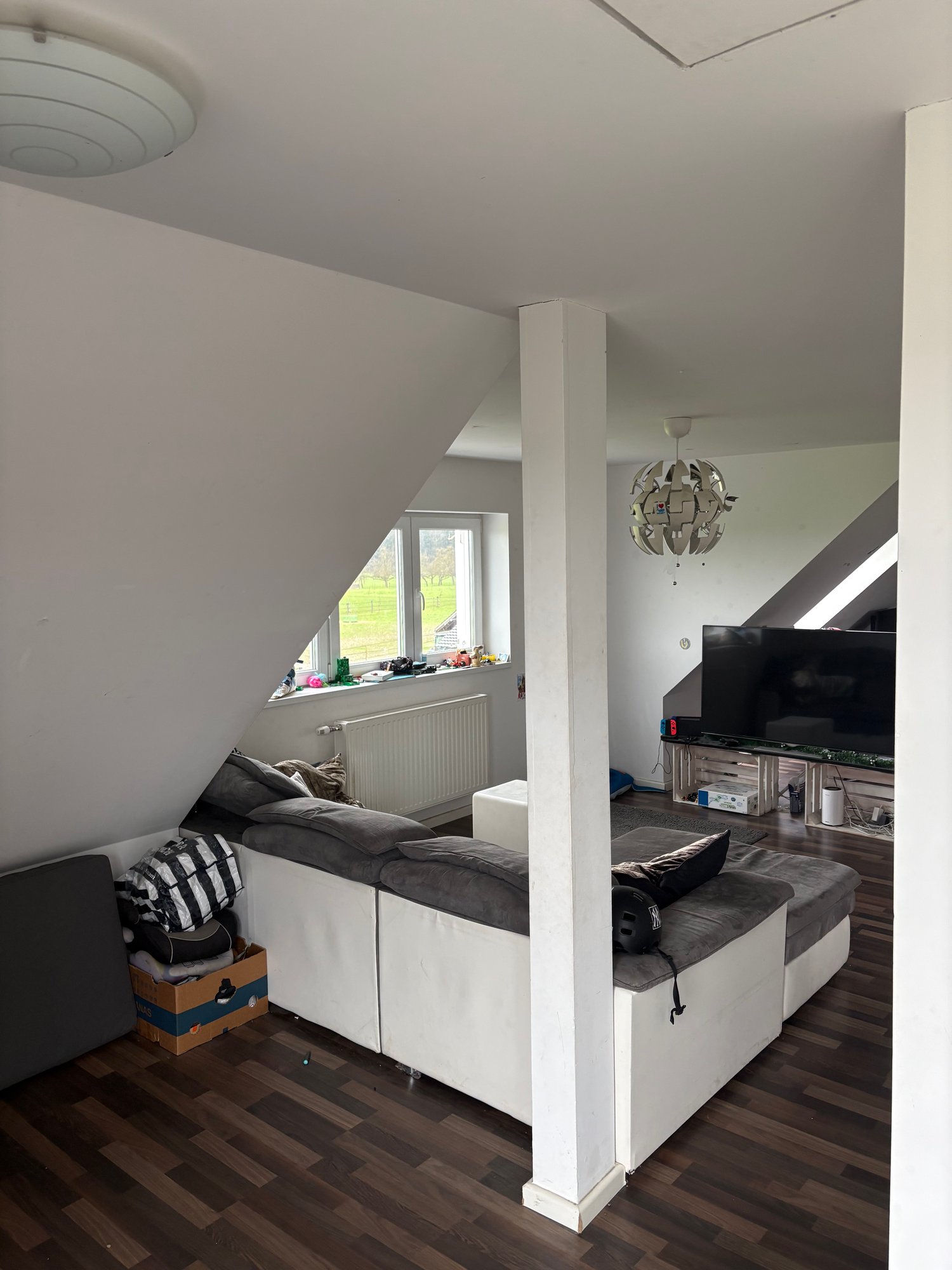 White couch, white ottoman, lamps, tv, wooden floor, window, wooden shelves, boxes
