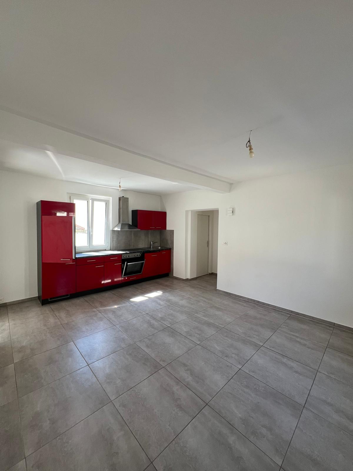 Empty kitchen with red cabinets, gray tiled floor, white walls, window, stove, sink, and a lamp