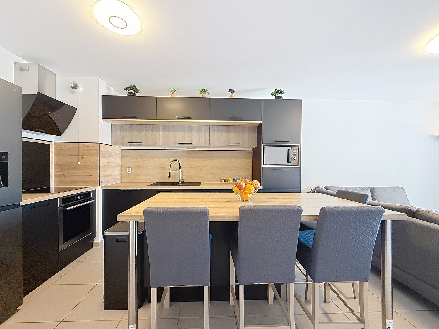 modern kitchen with dining area, wooden countertops, black cabinets, stainless steel appliances, microwave, sink, faucet, dining table with chairs, couch, tiled floor