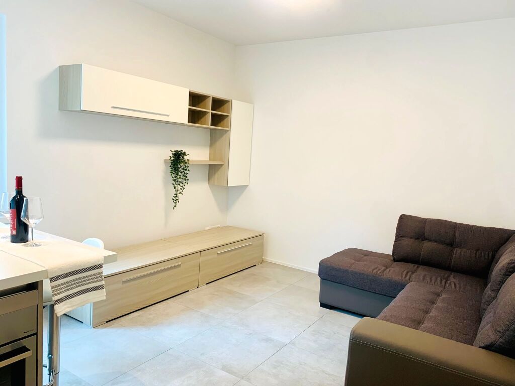modern living room with white walls, wooden floor, a couch, a bench, a wine bottle, wine glasses, a plant, and a white table
