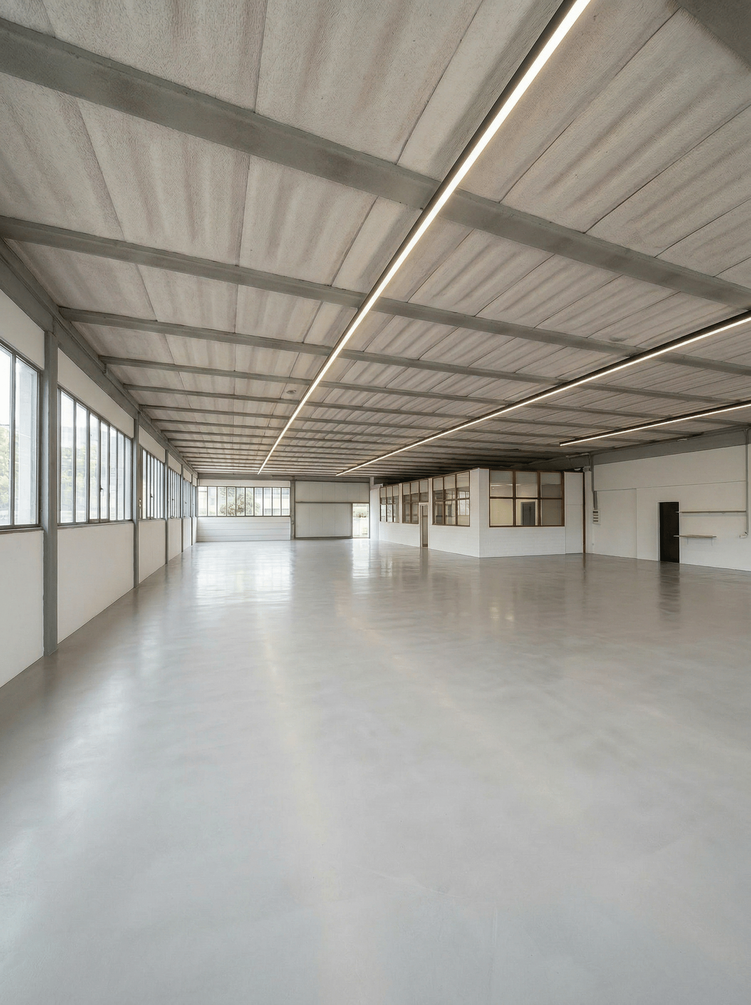 spacious room, white walls, concrete floor, large windows, metal beams, fluorescent lighting