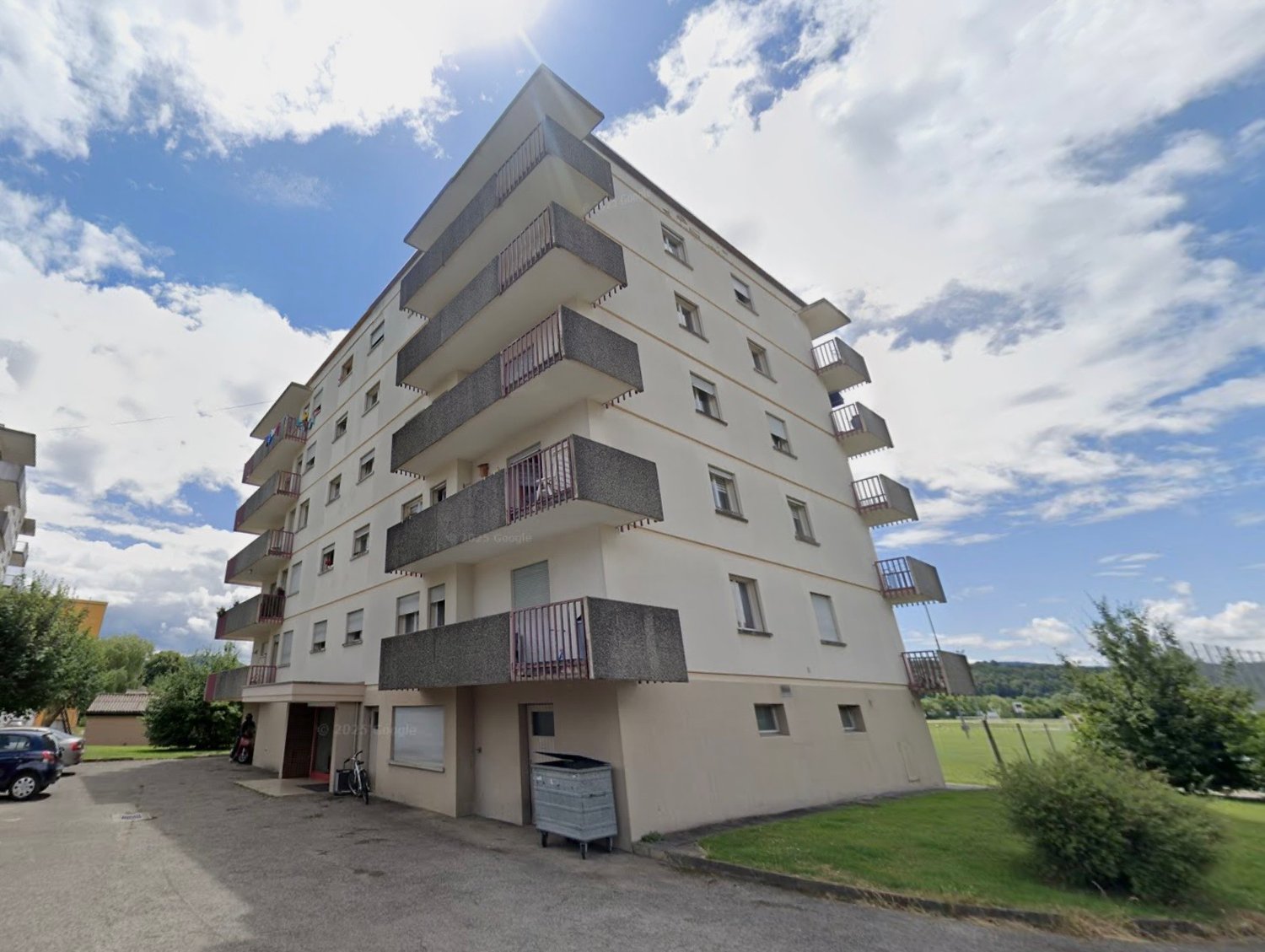 multi-story building, balconies, parking area, trash bin, trees, cars parked