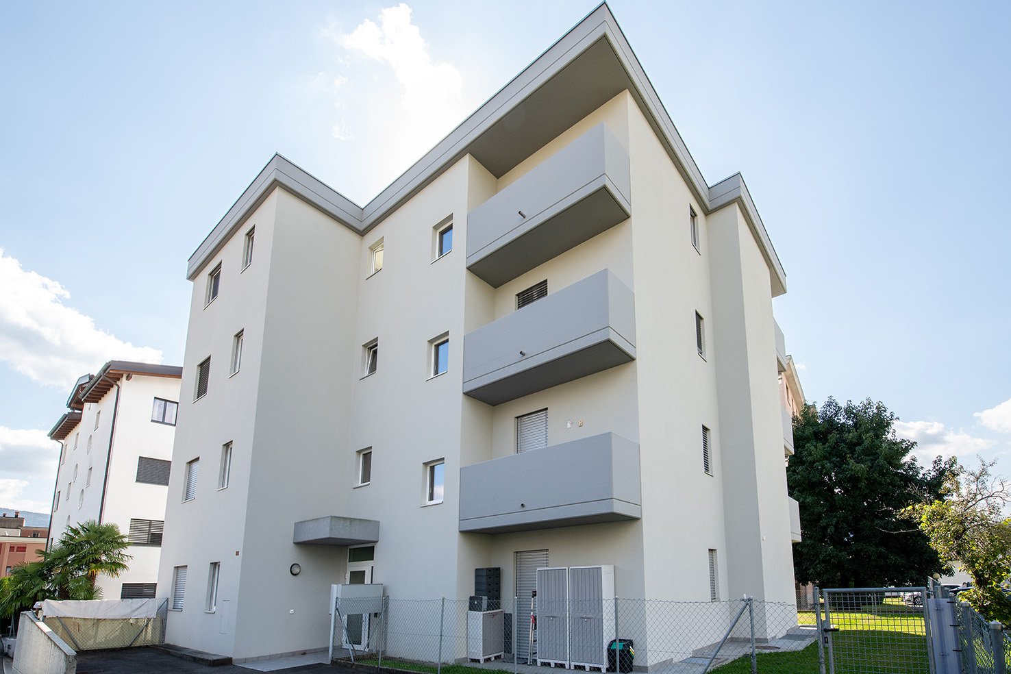 Modern white building, multiple balconies, multiple floors, fenced area in front
