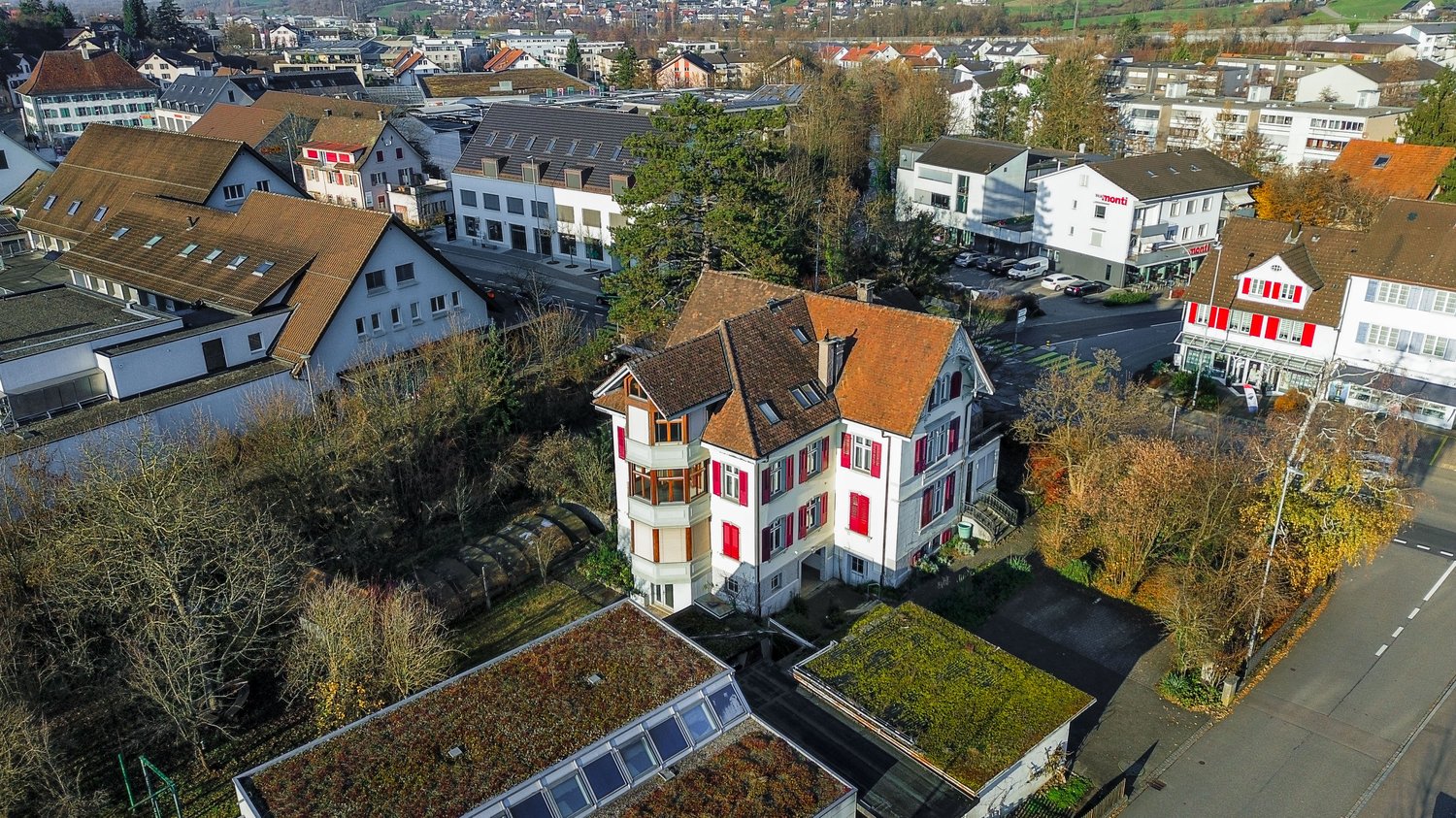 Two story house with brown roof, red windows, balcony, small garden