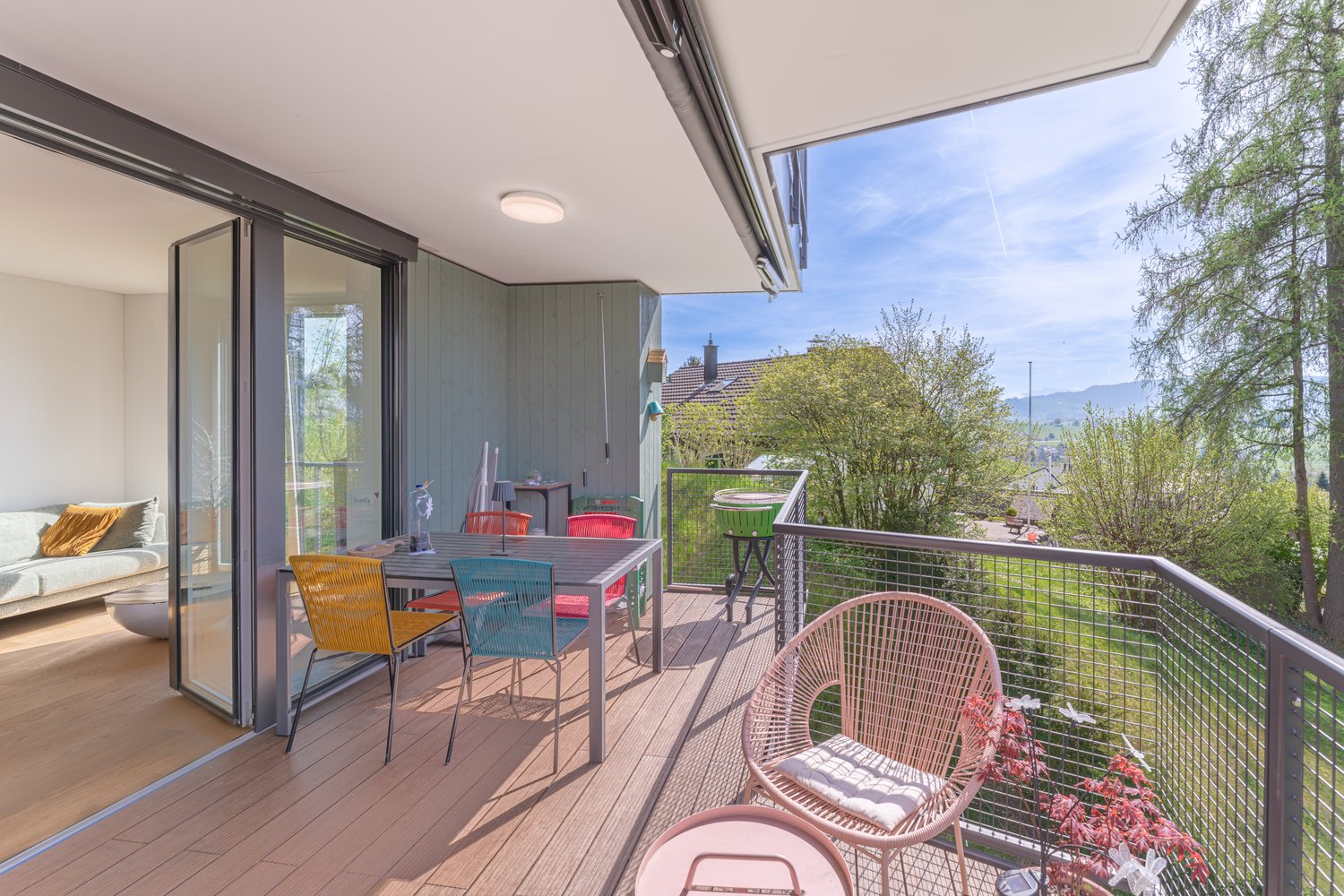 Balcony with wooden floor, metal railing, table and chairs, glass doors, couch, view of trees and mountains