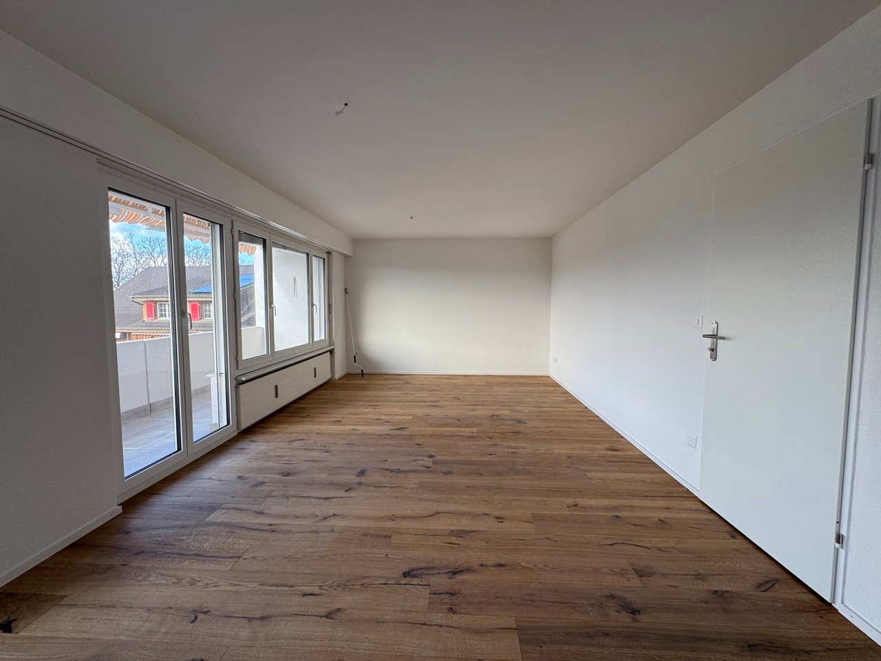 Spacious living room with large windows, hardwood flooring, and a minimalist design.