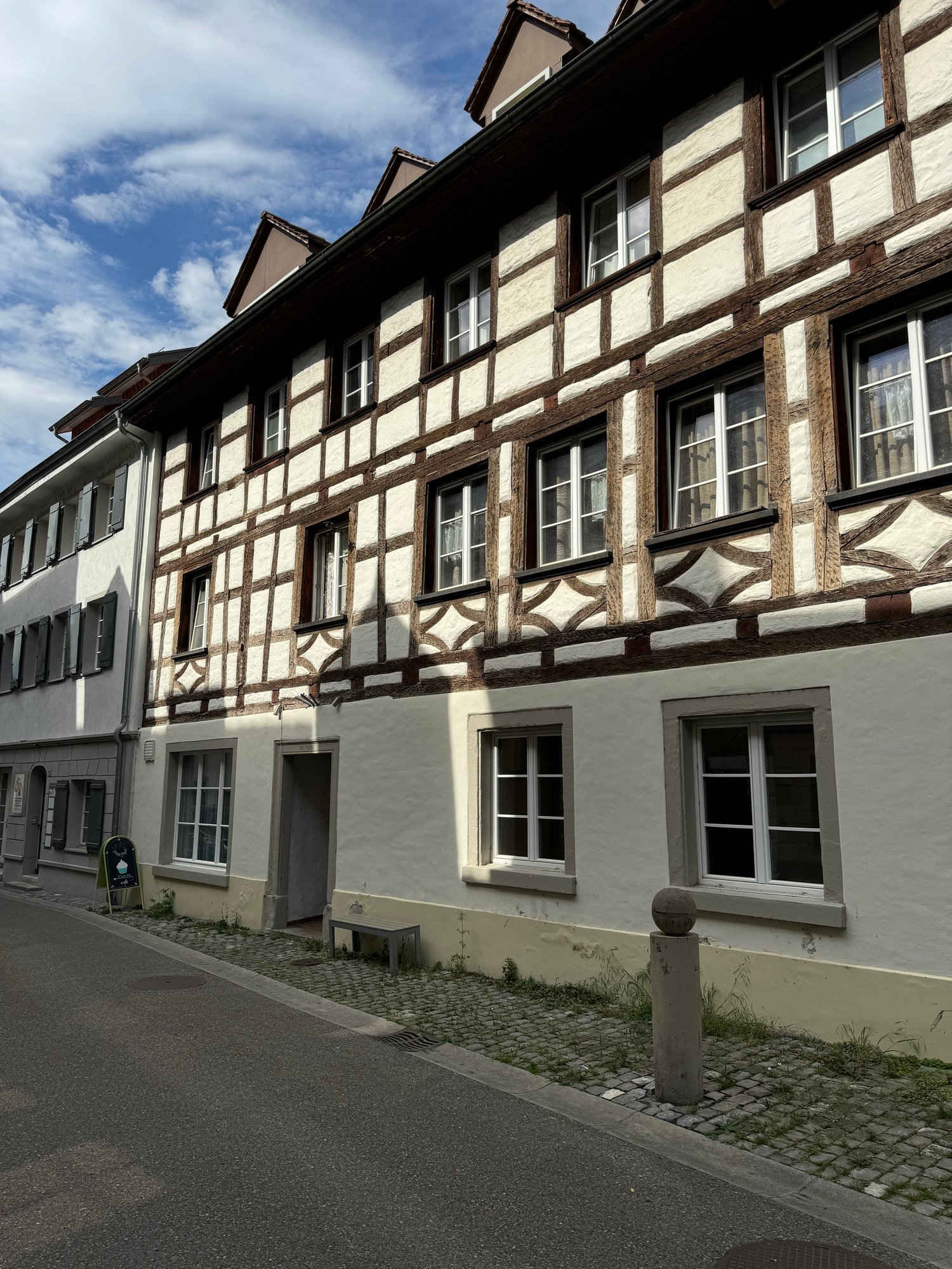 A traditional half-timbered building with white walls and dark wooden beams. The building has multiple floors and windows, and there is a cobblestone path in front of the building.