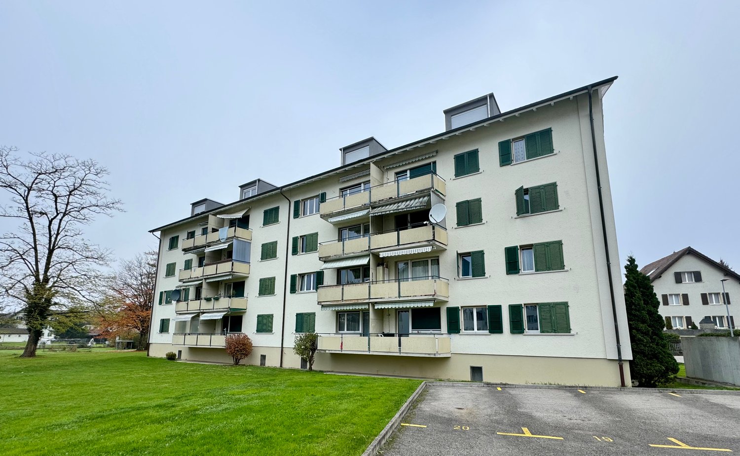 Multi-story apartment building with green shutters, balconies, and a grassy area in front