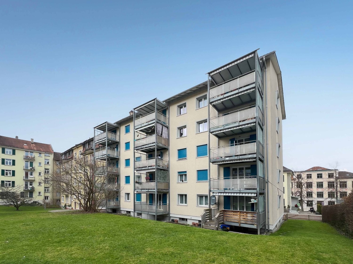 Large beige apartment building with multiple balconies and windows, grass lawn in front of the building