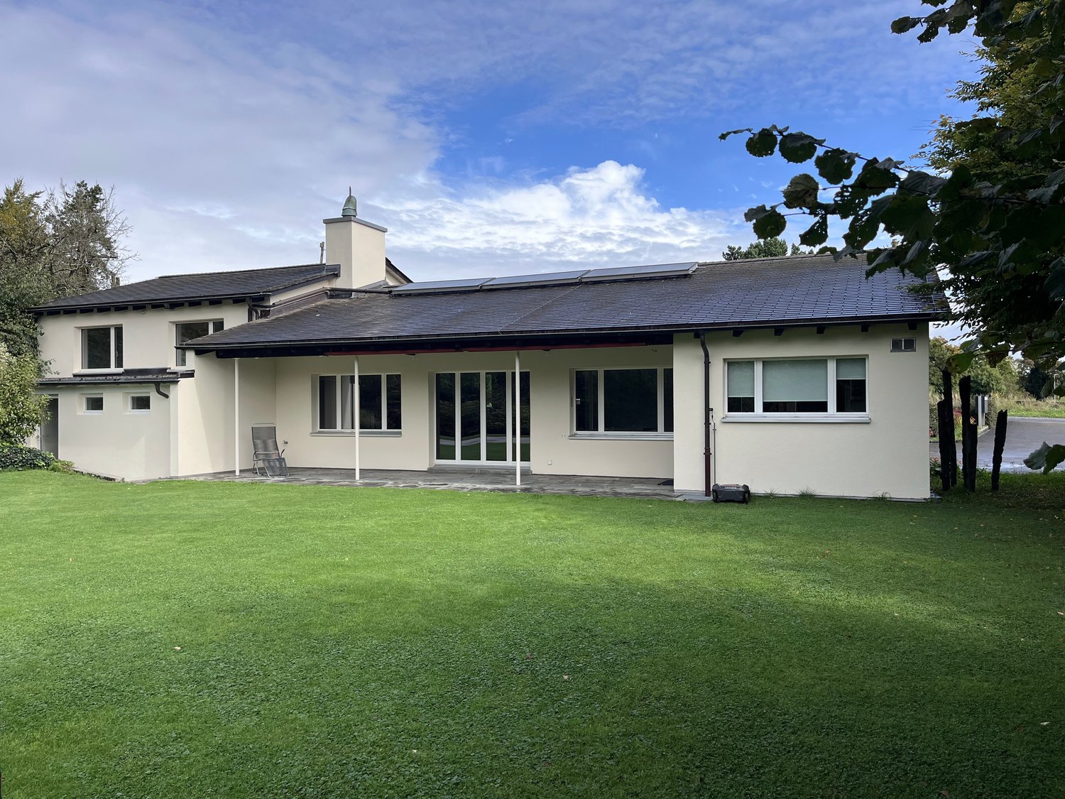 Modern white house with solar panels, large windows, sliding glass doors, lawn with trees