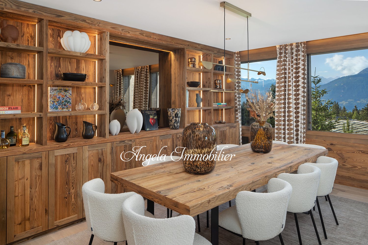 Dining room with wooden table, white chairs, wooden shelves, large windows, mountain view