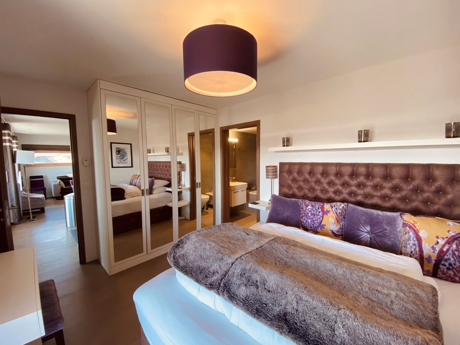 Bedroom with a large bed, a large wardrobe, a mirror, a lamp, a desk, and a chair.