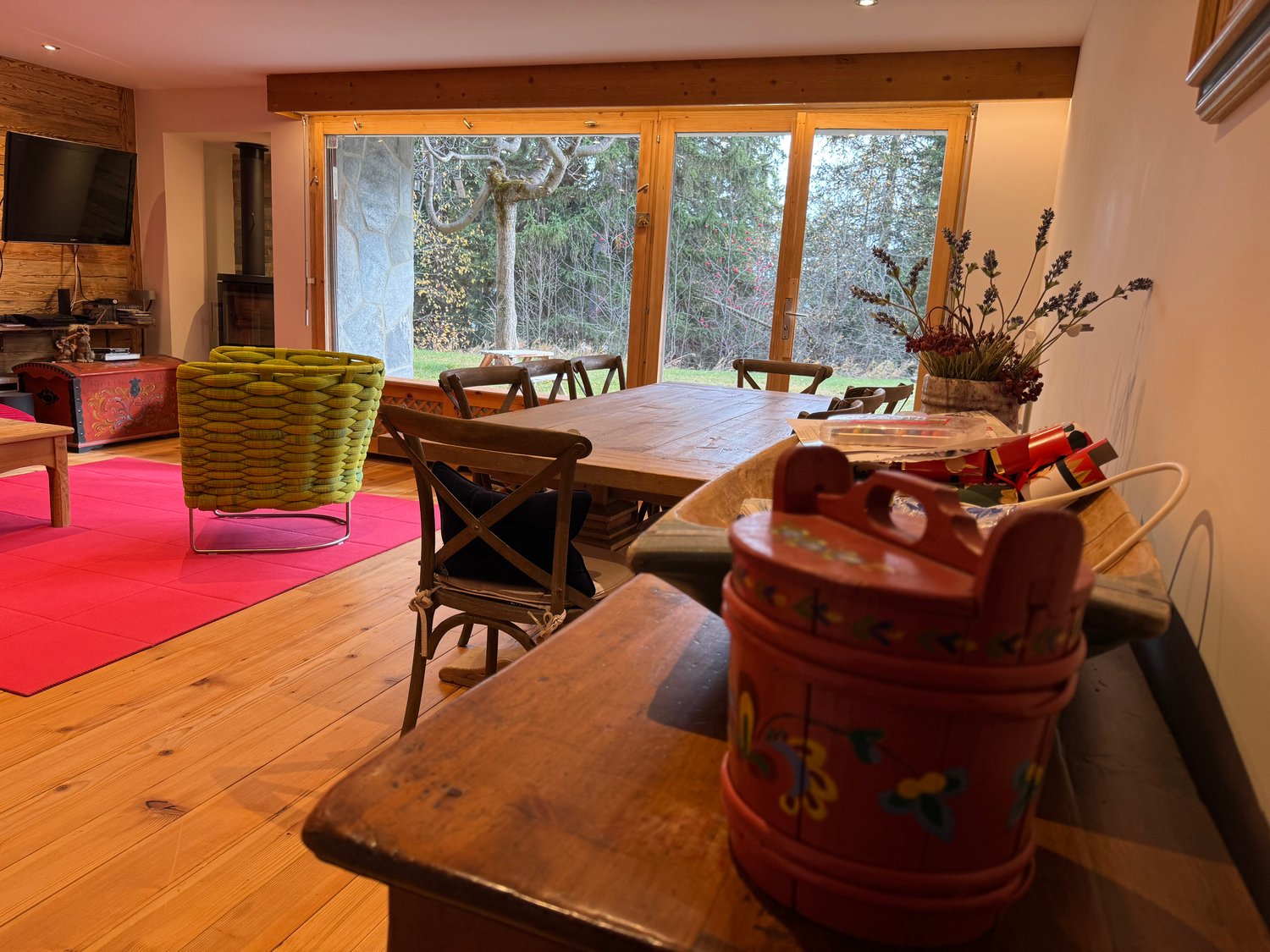 Wooden floor, dining table, chairs, TV, large glass doors, red carpet, decorative items, flowers