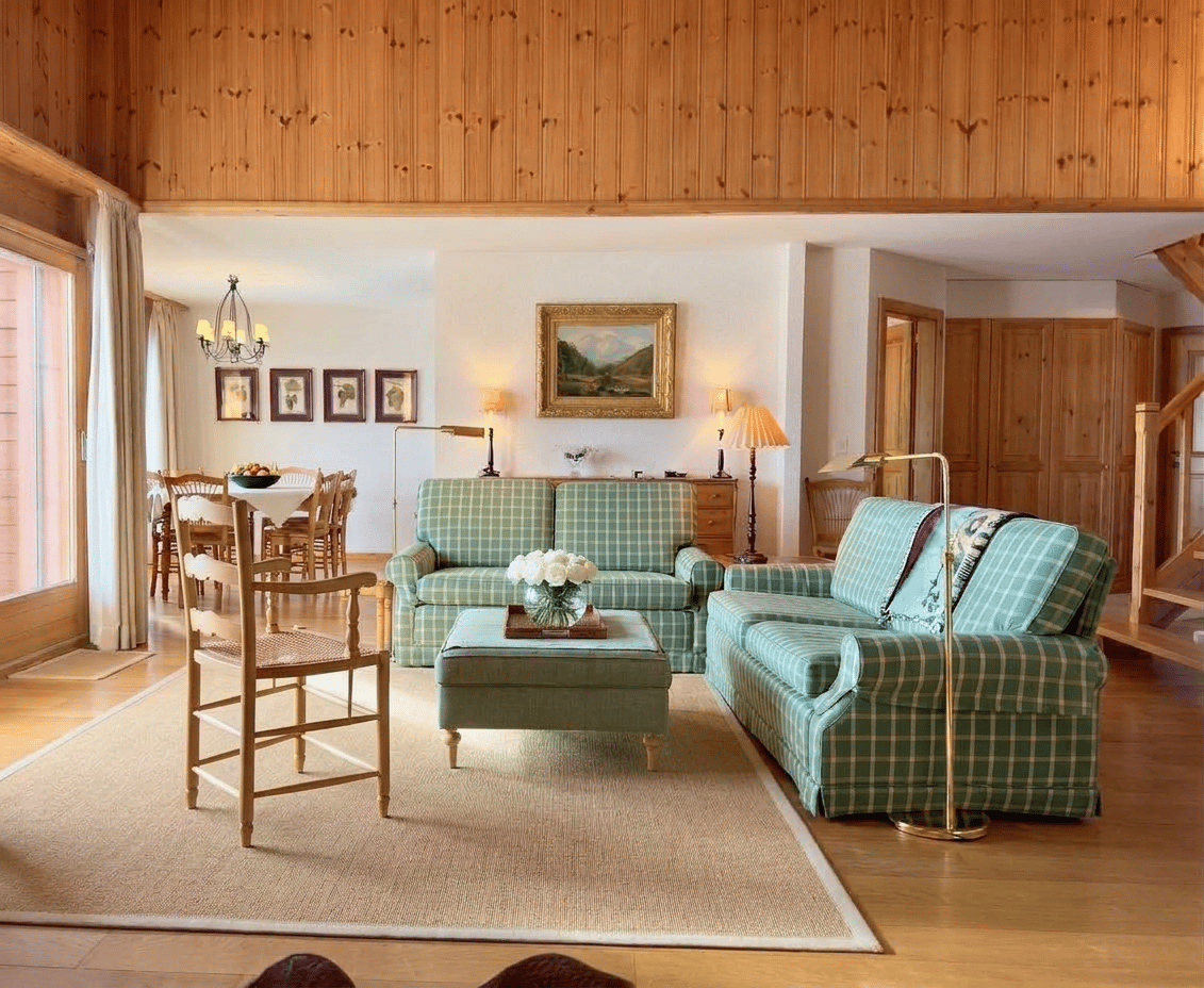 living room with wooden ceiling, green and white checkered sofas, wooden table, wooden chair, wooden floor, dining table and chairs, wooden cabinet, lamps, picture frames, chandelier