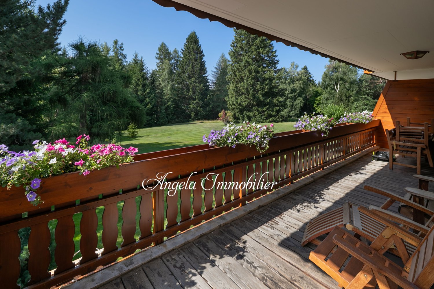 Wooden deck with railing, surrounded by lush greenery and flowers. Scenic view of the forest and open grassy area.
