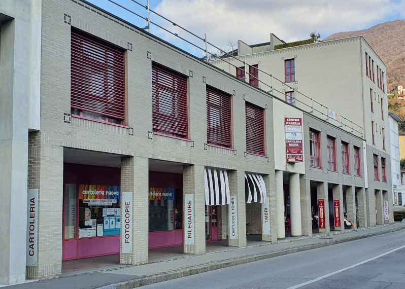 Two-story building, brick construction, red shutters, signage for various shops, multiple entrances