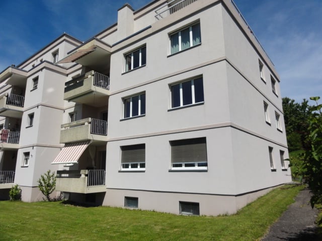 3-story apartment building with gray exterior, balconies, and windows