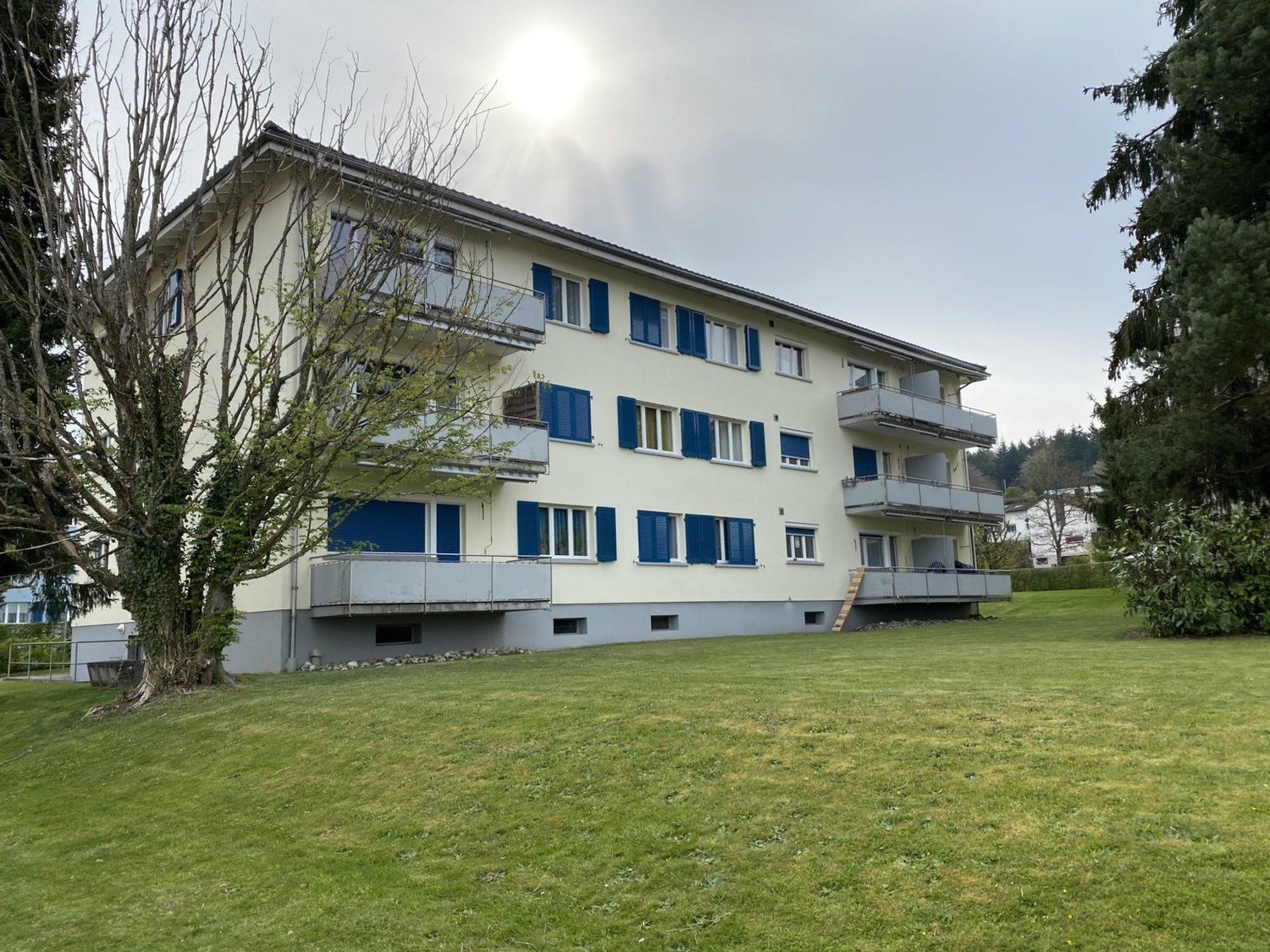 3 story apartment building, white walls, blue shutters, balconies, large grassy area