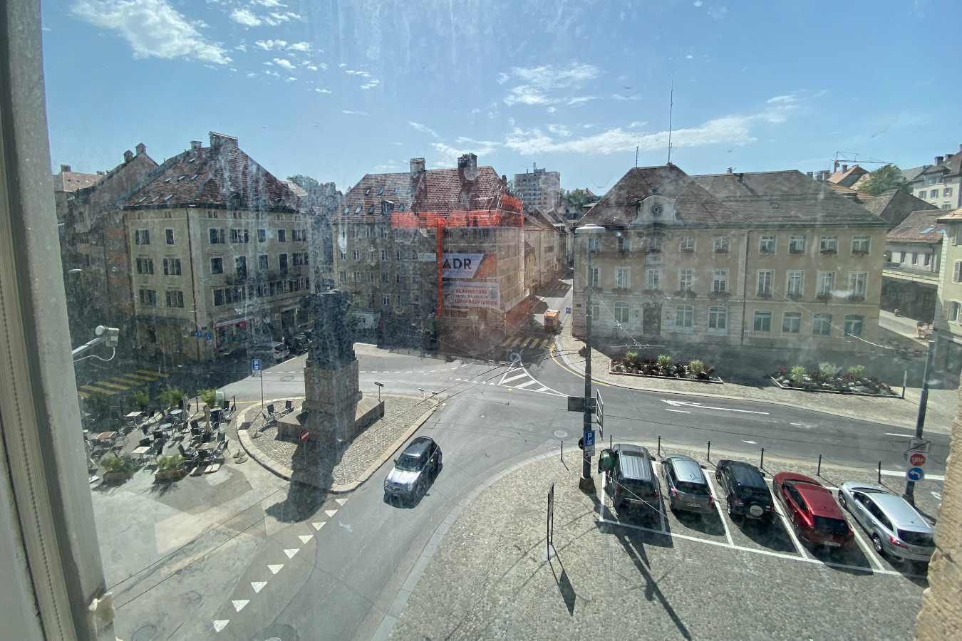Aerial view of a building with multiple floors overlooking a roundabout, a parking area, and adjacent street with parked cars