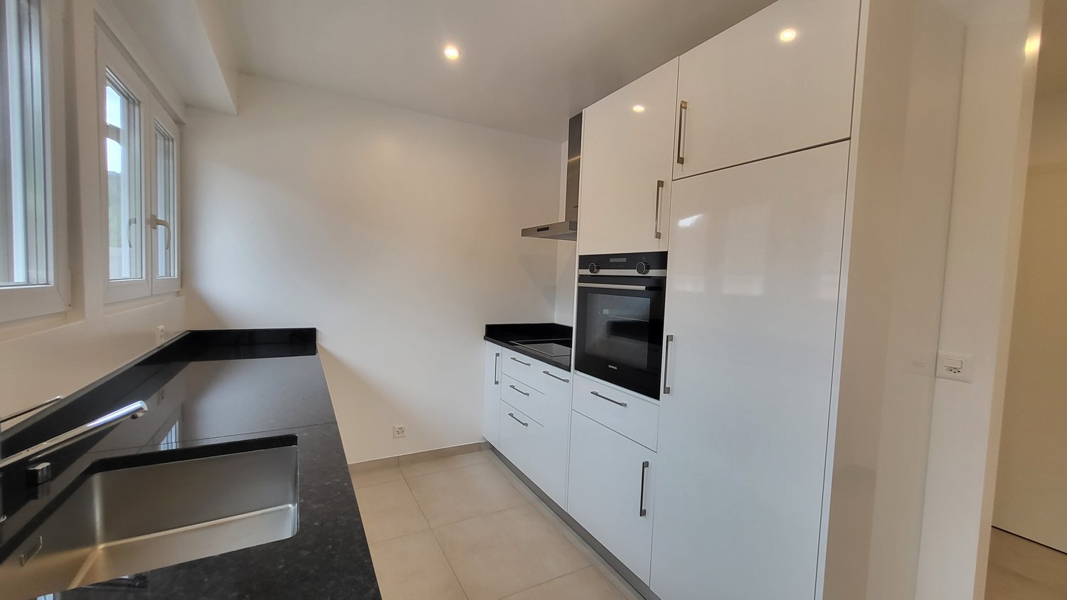 modern kitchen with white cabinets, black countertops, stainless steel sink, built-in oven and dishwasher, windows