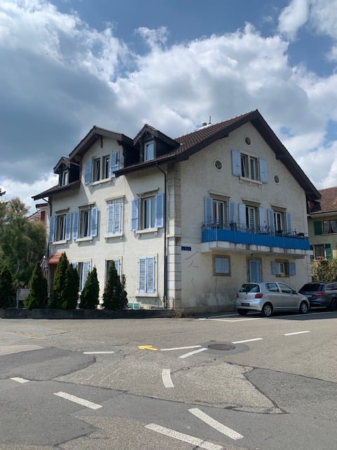 3-story residential building with white exterior, blue balconies, and parked cars in the front
