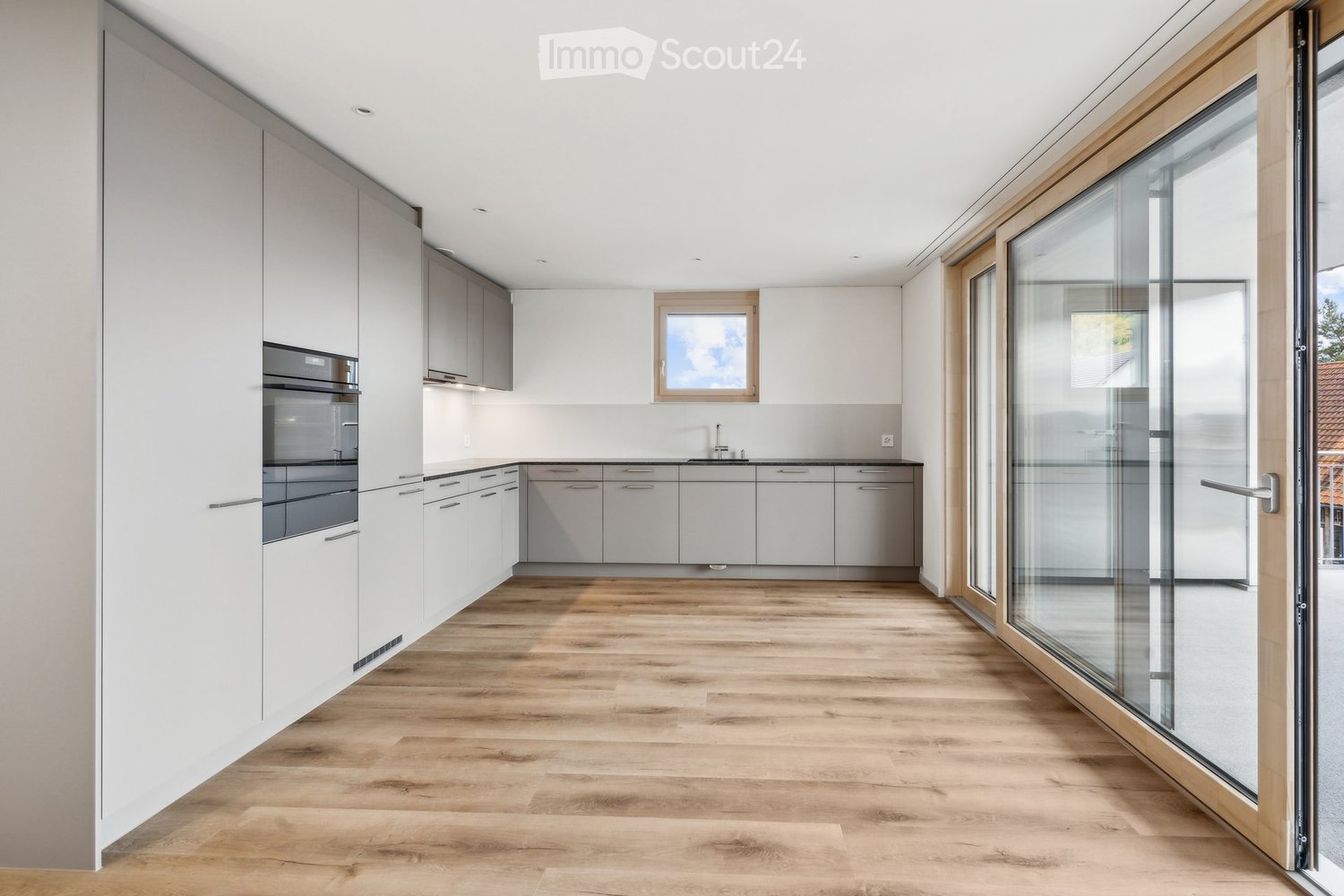 empty kitchen with wooden floor, glass sliding doors, white cupboards, window, modern design