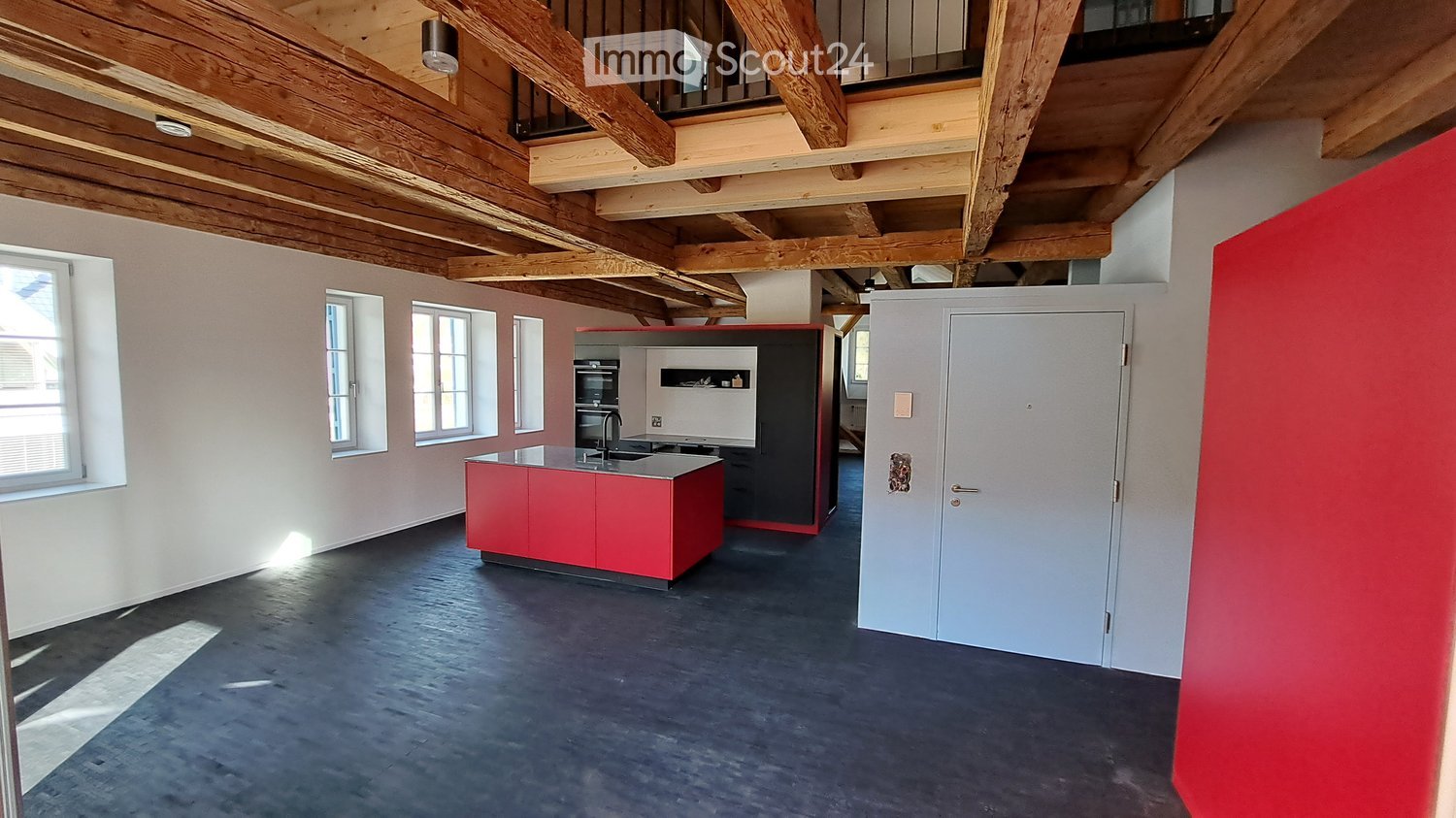 Large open-concept loft space with exposed wooden beams and ceiling, red kitchen island, black appliances, and hardwood flooring