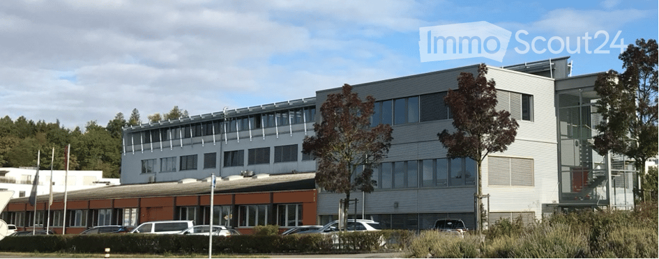 Modern multi-story building with glass windows, brown painted lower floor, several cars parked in front