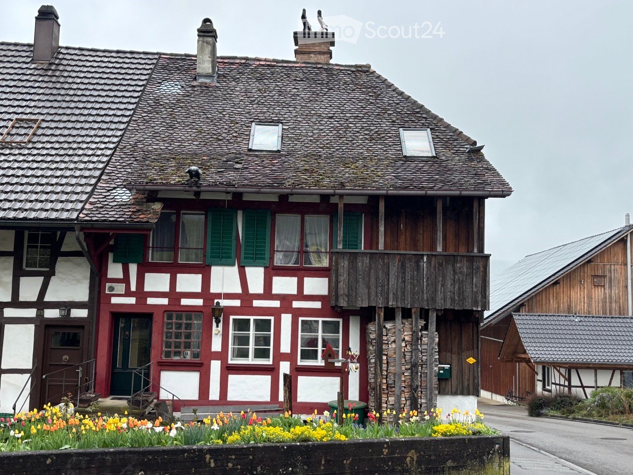 Traditional German half-timbered house, red and white, with wooden balcony, chimneys, and flowers in the front