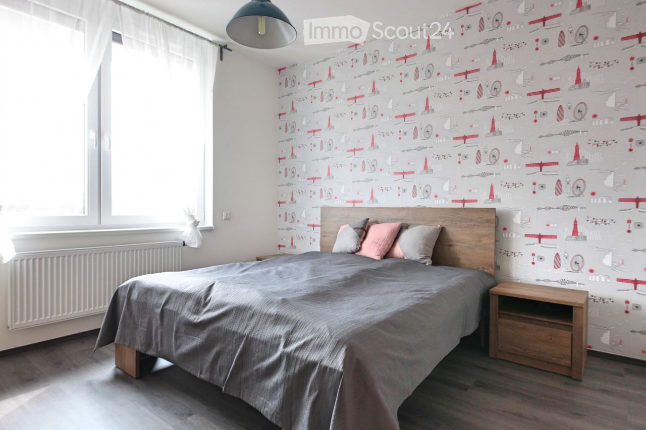 bedroom, double bed with gray sheets, light brown headboard, two bedside tables, radiator, gray wallpaper with red pattern