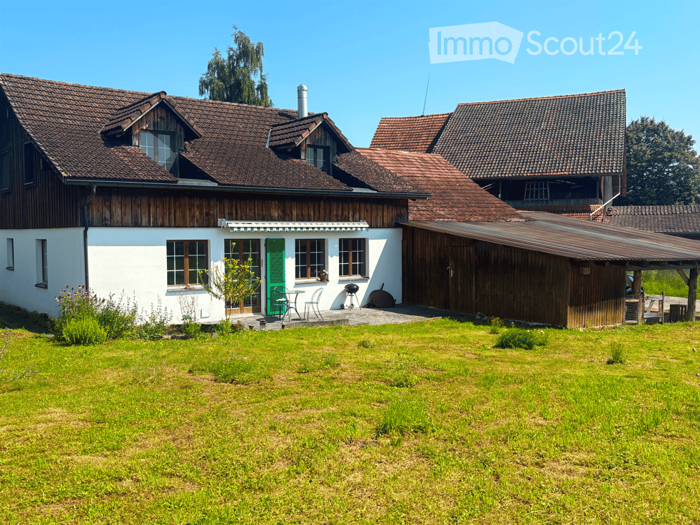 Two story house, brown roof, white walls, wooden garage, grassy field