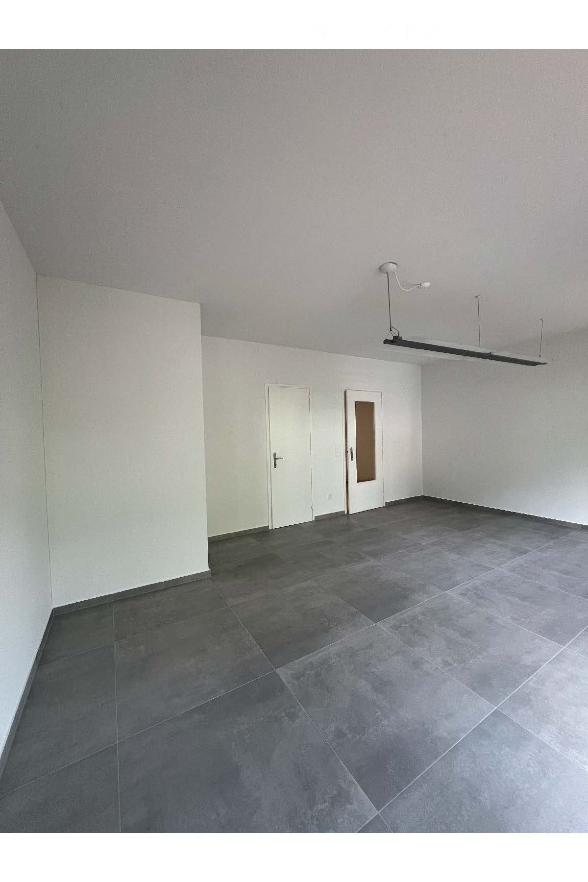 Large, empty, white-walled room with grey tile flooring and two doors