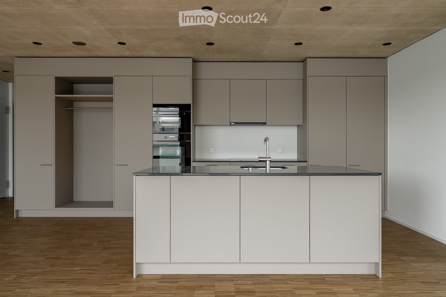 island with sink and faucet, built-in double oven, wooden floor, white walls, kitchen cabinets