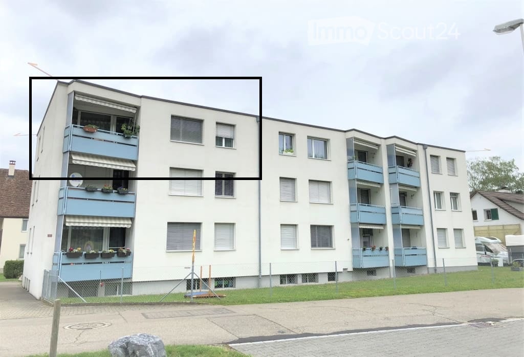 4 story apartment building, white exterior, blue balconies, fenced area, grass lawn, paved sidewalk