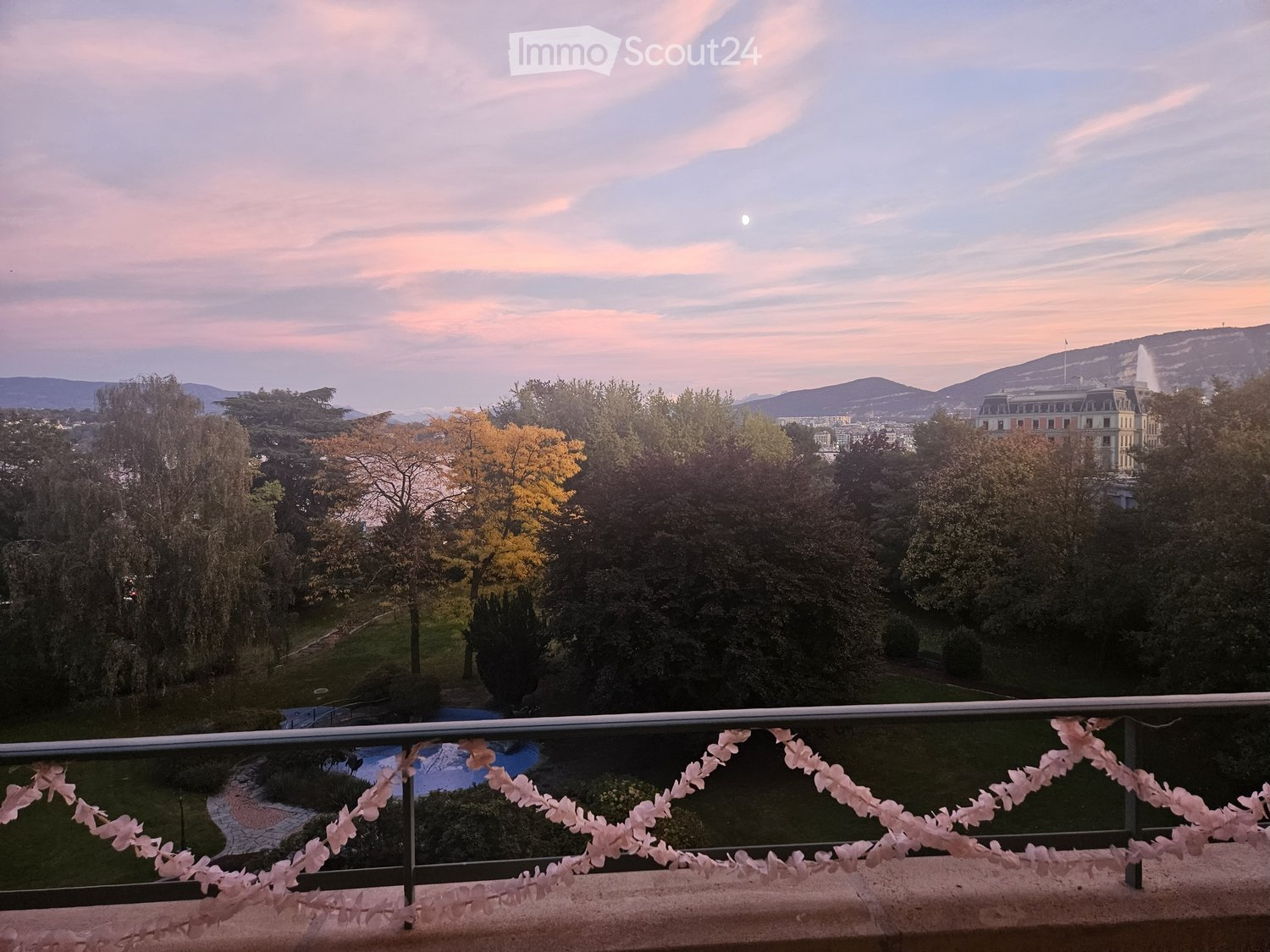 balcony with railing, view of trees, fountain, mountains, sky, sunset
