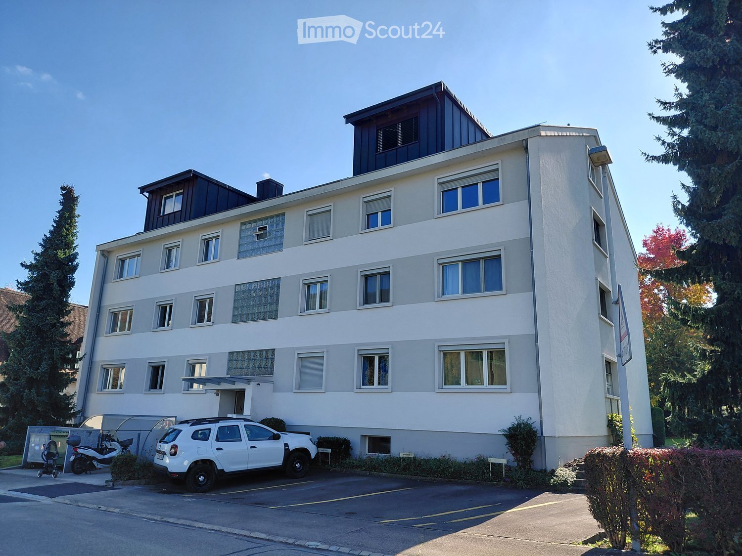 4 story white building, grey accents, many windows, parking spaces, scooters parked in front