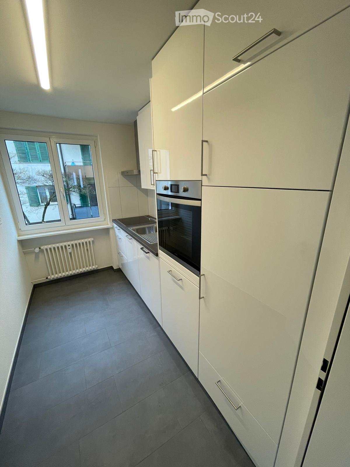 modern kitchen with built-in appliances, white cabinets, black floor, window with shutters