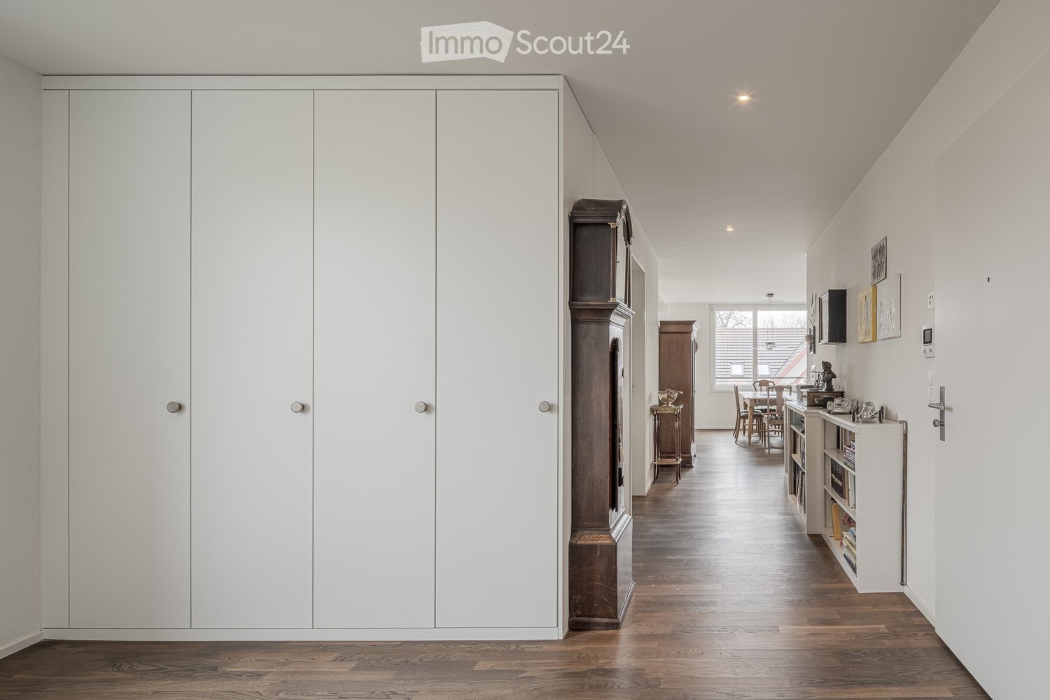 Corridor with large wooden cabinets and a grandfather clock. Long hallway with wooden flooring.