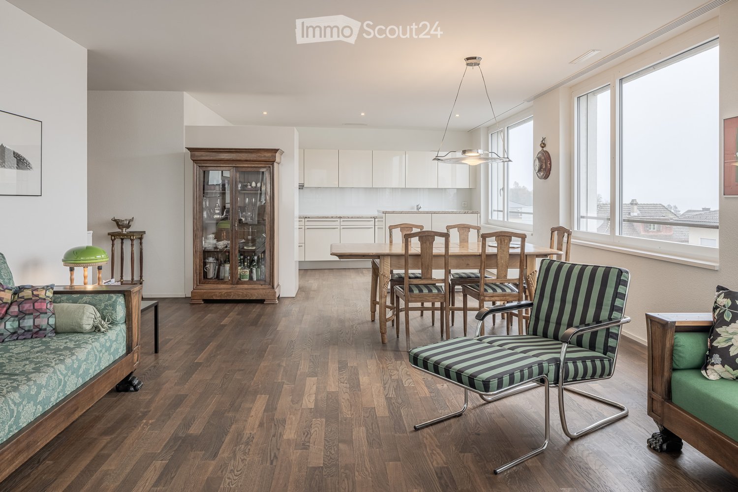 open-plan living room and dining area with wooden floor, white walls, modern furniture, glass cabinet, large windows, hanging lamp, wooden table and chairs