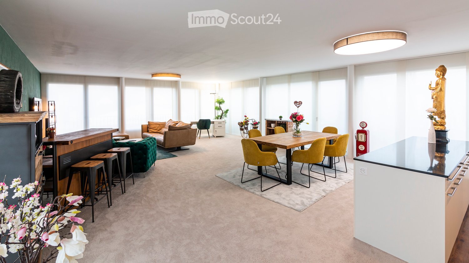 Large open space with living room and dining area, wooden table with chairs, sofas, center table, side table, ceiling lamp, carpet, flower arrangement, wooden cabinet